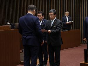 議場において高橋達総務財政常任委員長が市長に提言書を手渡す様子の写真